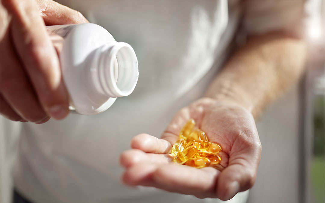 Person pouring supplement capsules from a white bottle into hand