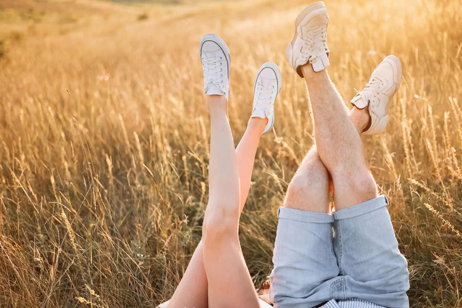 A man and woman sitting in a field with their legs up.