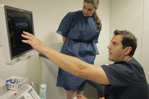 A doctor is pointing to an ultrasound while a woman is looking at it.