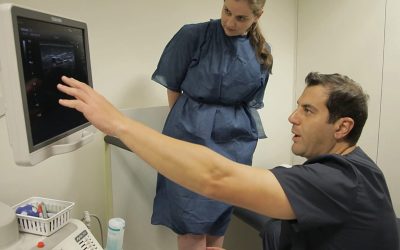 A doctor is pointing to an ultrasound while a woman is looking at it.