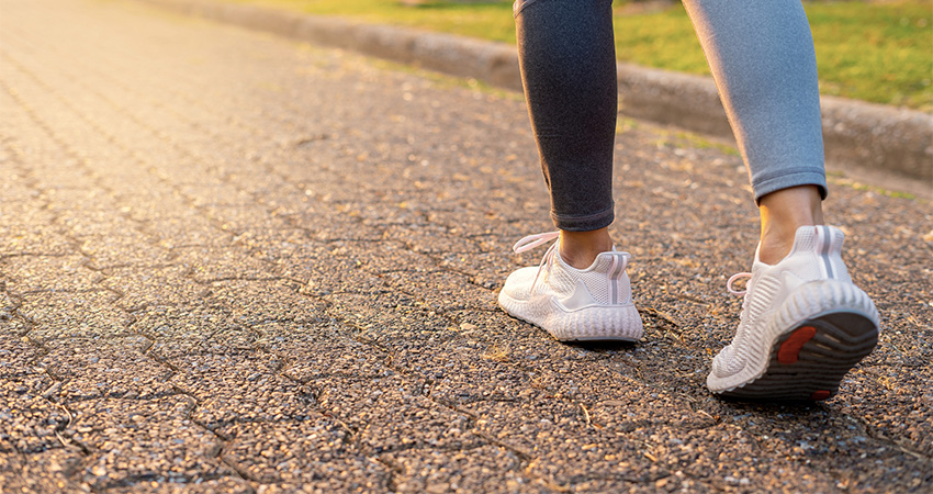 Close-up of a person walking on a sunlit paved path, wearing white athletic shoes and leggings—enjoy exercise after vein treatment.